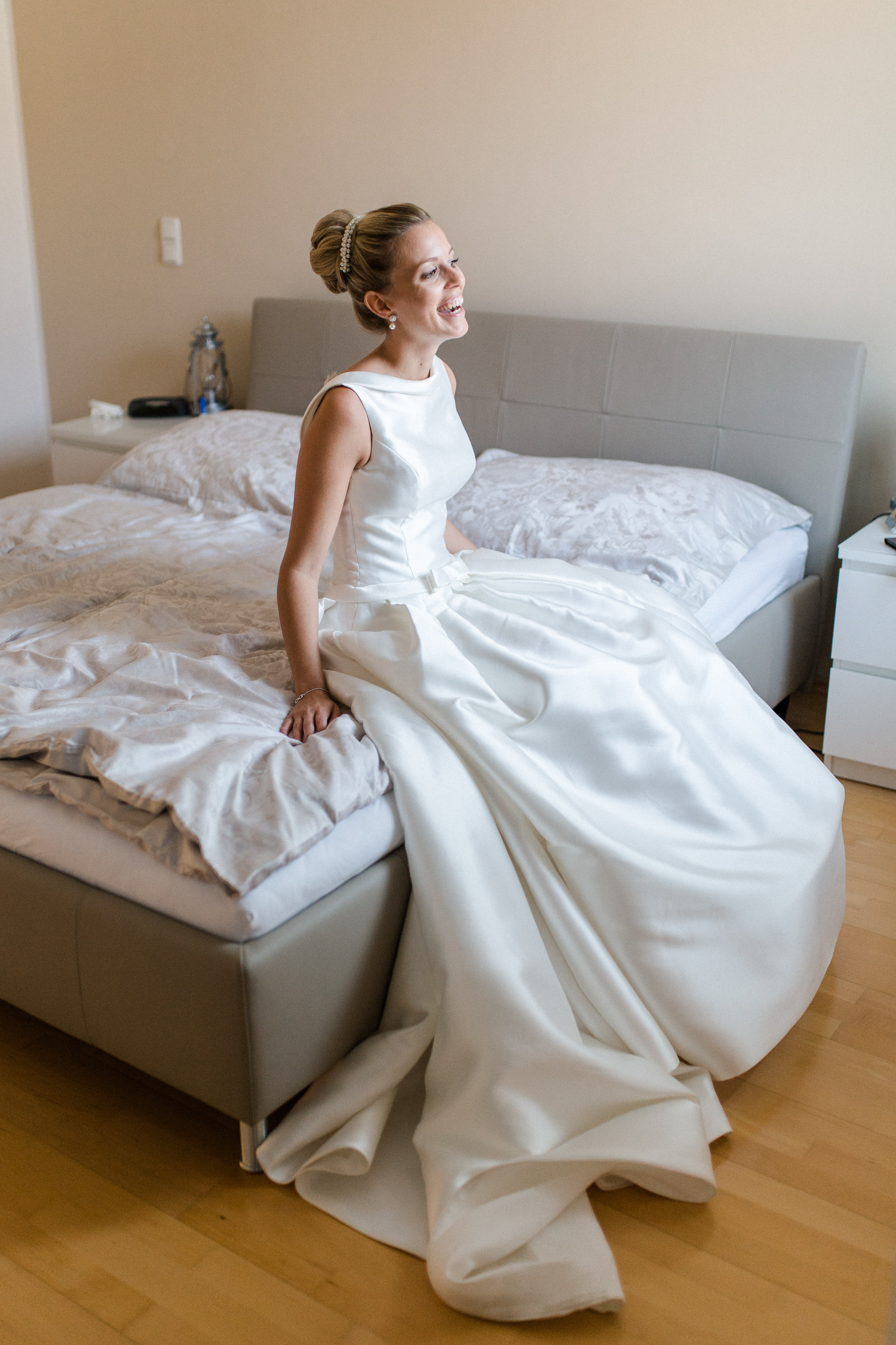 Braut sitzt glücklich und lachend am Bett